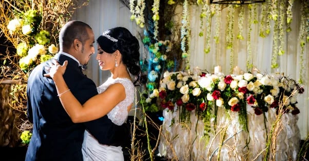 Bride and groom embracing during first dance at elegant wedding reception with gold lighting and colorful floral arrangements