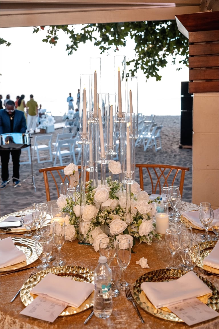 Elegant beachside wedding reception table with white floral centerpiece, candelabra, and ocean view in background
