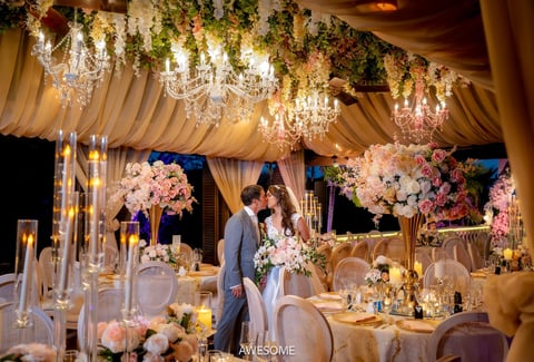 Elegant outdoor wedding reception at night with flowing fabric draping, crystal chandeliers, pink floral arrangements, and decorated tables under string lights