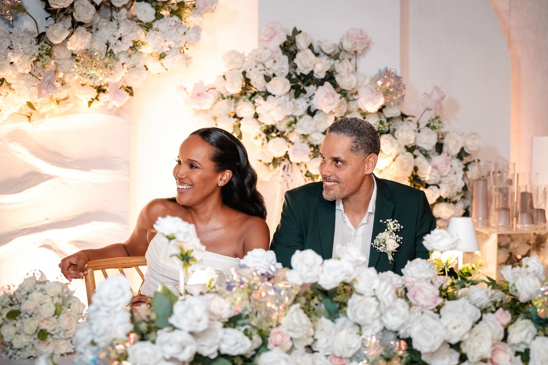 Bride and groom smiling at their wedding reception surrounded by white and pink floral arrangements and decorations