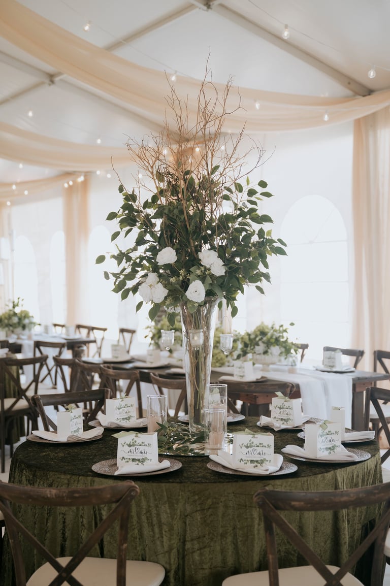 Elegant event centerpiece with tall floral arrangement featuring white flowers and dried branches on round table with green fabric