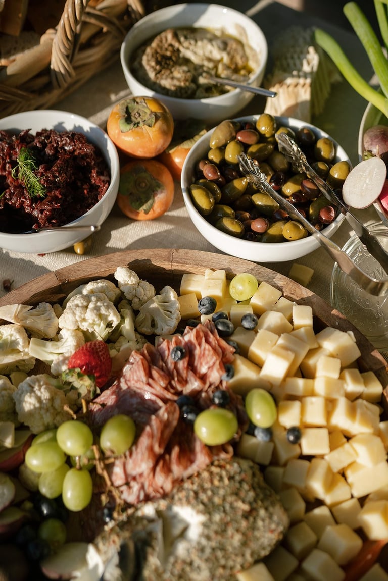 Overhead view of a charcuterie board with cured meats, cheeses, olives, grapes, and vegetables displayed on wooden and white serving plates