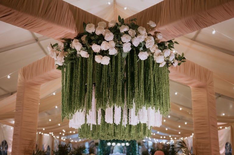 Elegant hanging floral installation with white flowers and cascading green foliage in an indoor venue with draped fabric ceiling
