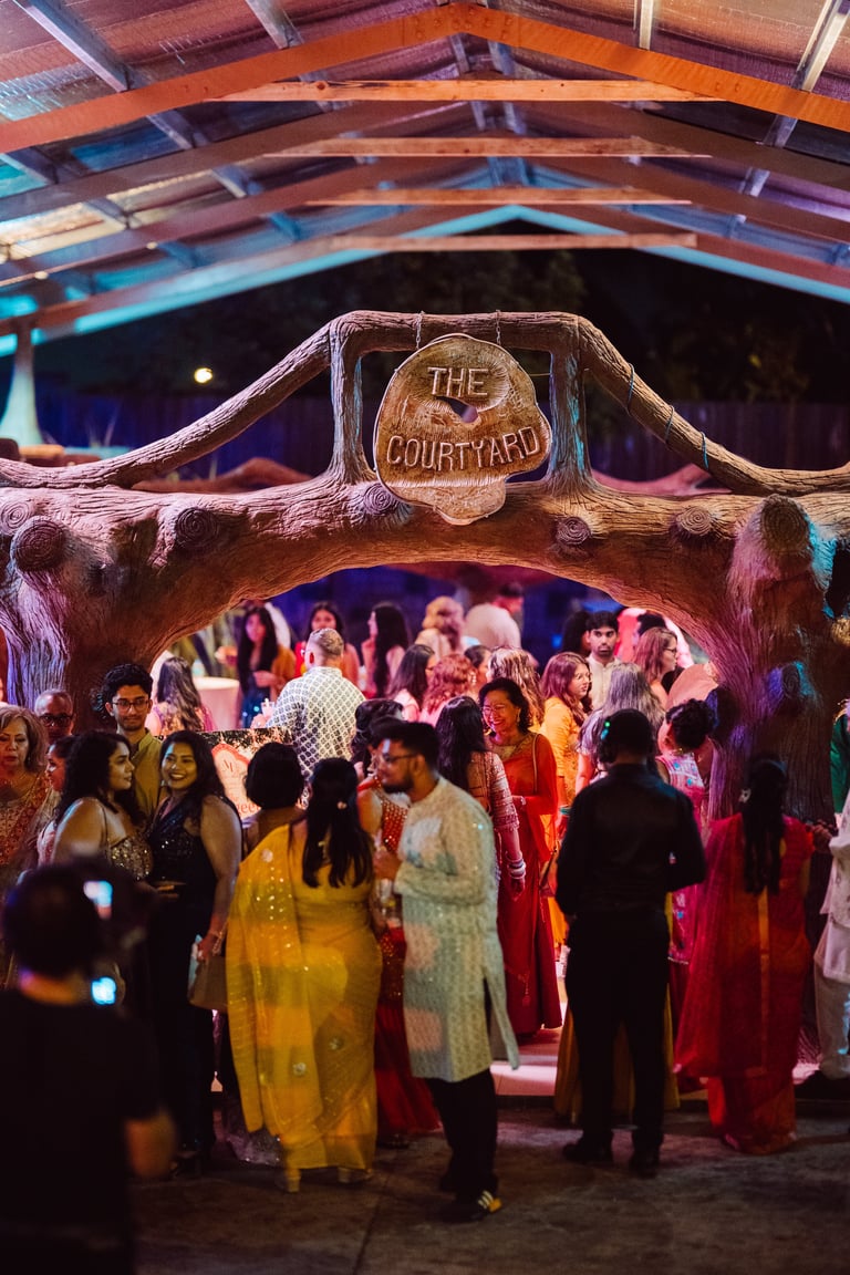 Guests gather at The Courtyard entrance decorated with wooden archway and colorful blue and orange beams overhead at an upscale event