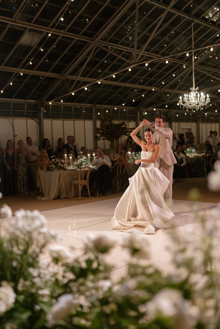 Bride and groom dancing at their wedding reception in an elegant indoor venue with white flowers and chandeliers