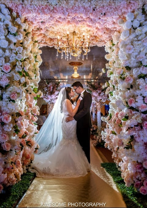 Bride and groom kissing under ornate floral arch at wedding ceremony with pink and white roses