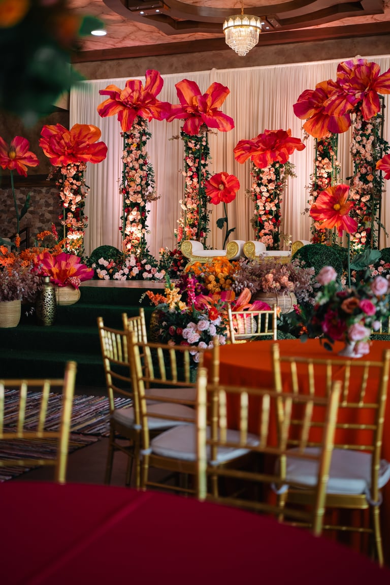 Elegant event venue with tall floral arrangements featuring red and pink flowers, gold chairs, and burgundy carpet