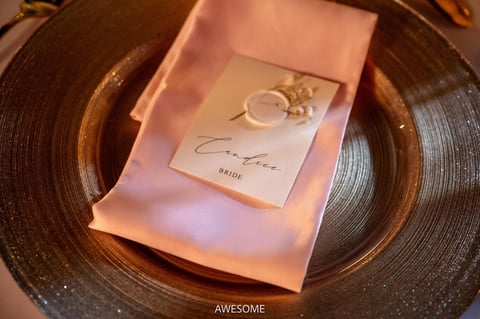 Place setting with pink napkin, wedding rings, and bride card on bronze charger plate