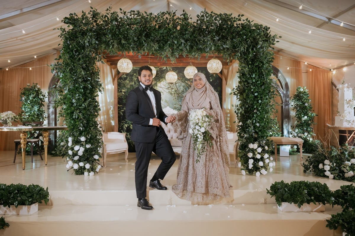 Couple dancing under floral arch decorated with greenery and hanging lanterns at an elegant indoor wedding venue