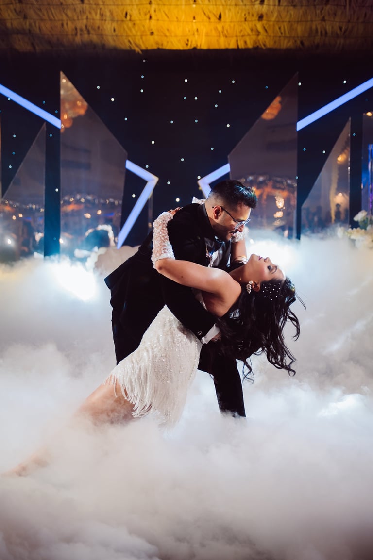 Groom dipping bride in his arms on a stage surrounded by dramatic fog and city skyline backdrop at night