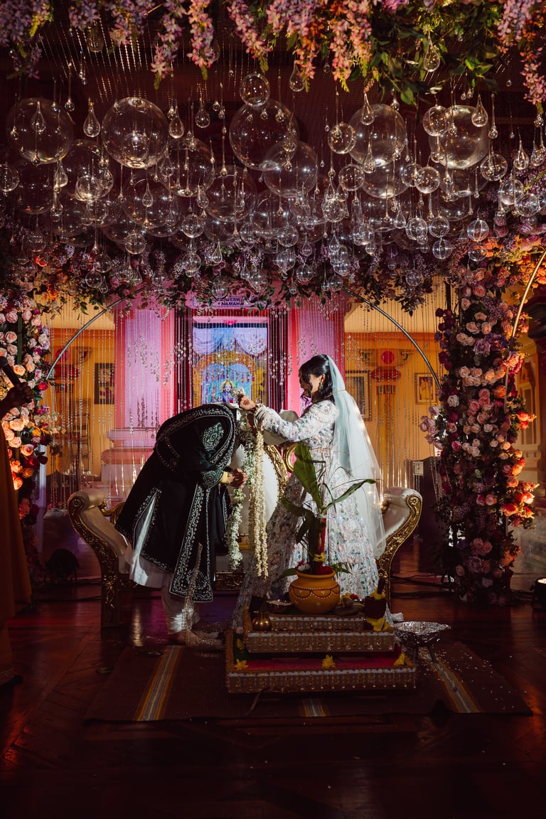 Bride and groom in traditional wedding attire standing before ornate floral backdrop with hanging crystals and decorated arch