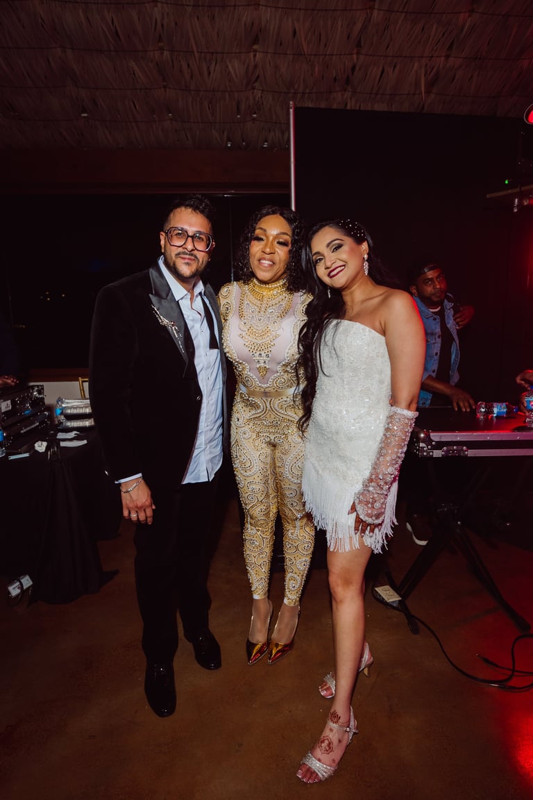 Three people posing together at an indoor event with stage lighting, wearing formal attire including gold and white sequined outfits