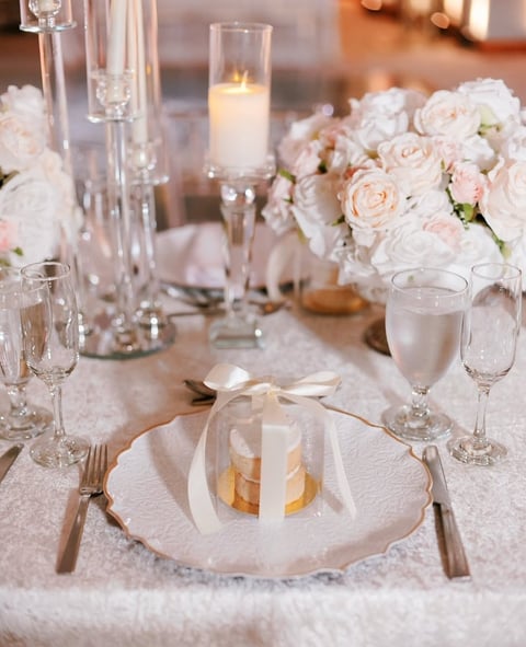 Elegant wedding table setting with white roses, place settings, candles, and champagne glasses on neutral linens