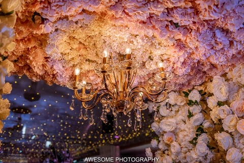 Ornate gold candelabra hanging beneath a stunning floral installation of pink and white flowers with warm and cool lighting