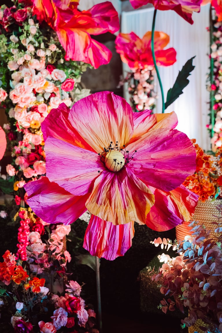 Large colorful artificial cosmos flower with pink and orange petals surrounded by smaller decorative flowers in various colors