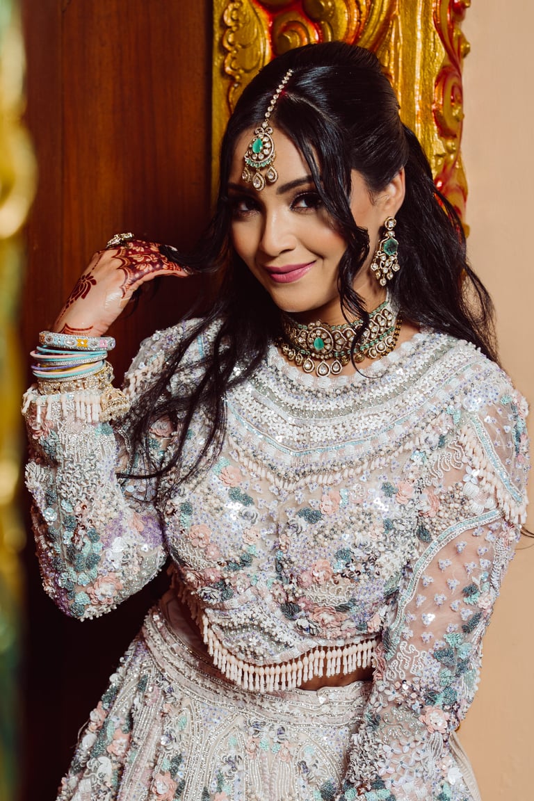 Woman wearing ornate beaded Indian bridal lehenga with jewelry and bindi, posing against golden framed backdrop