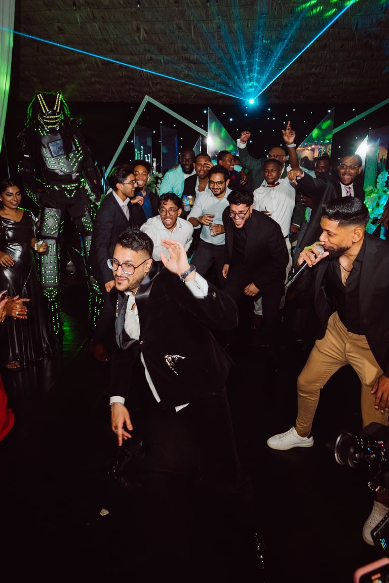 Group of men in formal attire dancing and socializing at a nightclub with neon green and blue laser lights