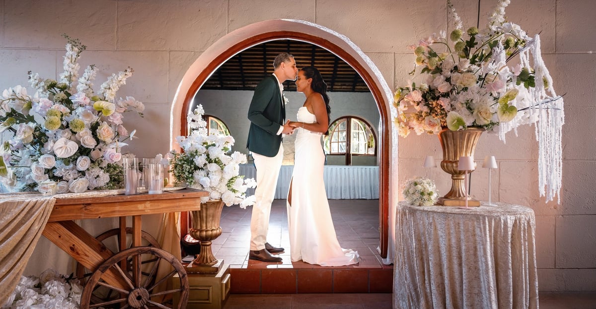 Bride and groom posing in an arched doorway decorated with white and blush floral arrangements and draped fabrics