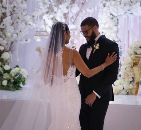 Bride and groom embrace at wedding altar surrounded by white floral decorations and greenery