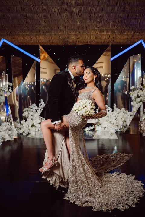 Bride and groom embrace on stage surrounded by white flowers and blue neon lights during wedding reception
