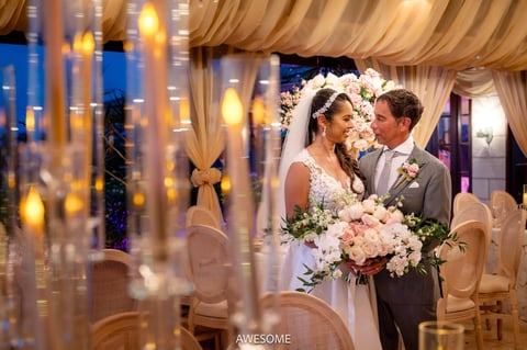 Bride and groom sharing a kiss at their elegant wedding reception, surrounded by white floral arrangements and draped fabric.
