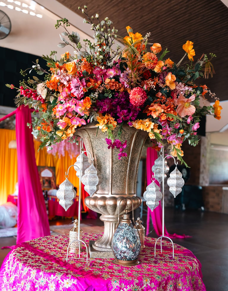 Ornate floral arrangement in large decorative urn with hanging crystals on pink sequined table at event venue