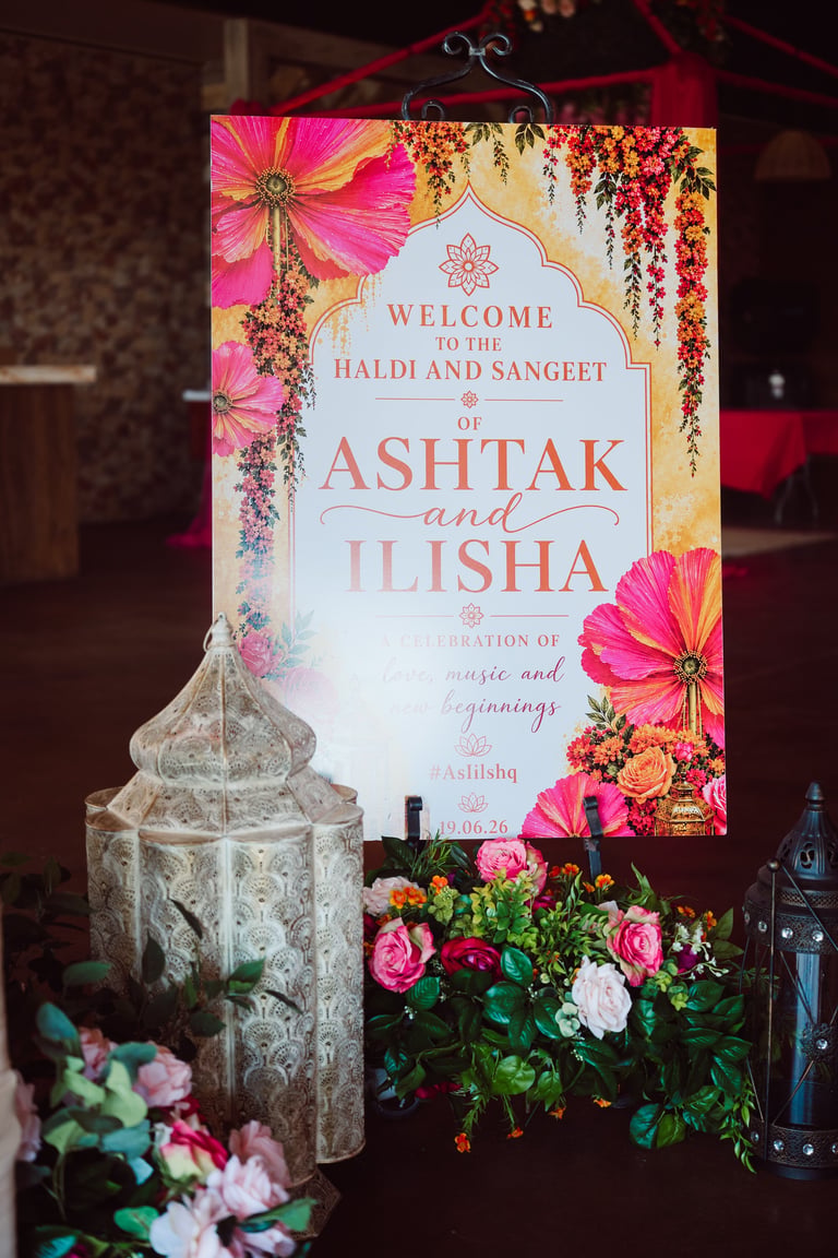 Wedding welcome sign for Ashtak and Ilisha with decorative pink flowers, hanging lantern, and floral arrangements