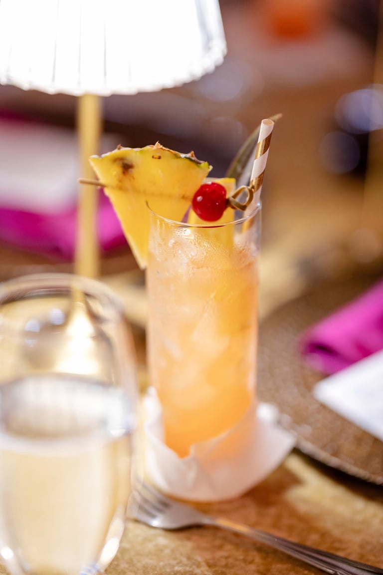A tropical cocktail with pineapple and cherry garnish served in a tall glass with ice at an upscale restaurant.