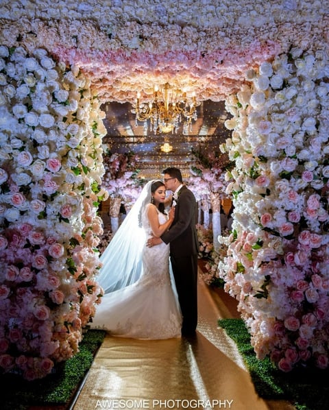 Bride and groom kiss under a floral arch covered in white and pink flowers at a luxury wedding ceremony