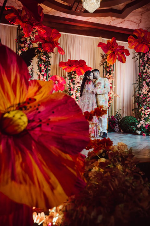 Elegant wedding ceremony venue decorated with oversized red flowers, floral installations, and ornate draping with couple standing at altar