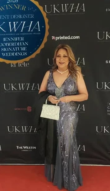 Woman in gray sequined dress holding white clutch on red carpet at UKWHA event with branded backdrops