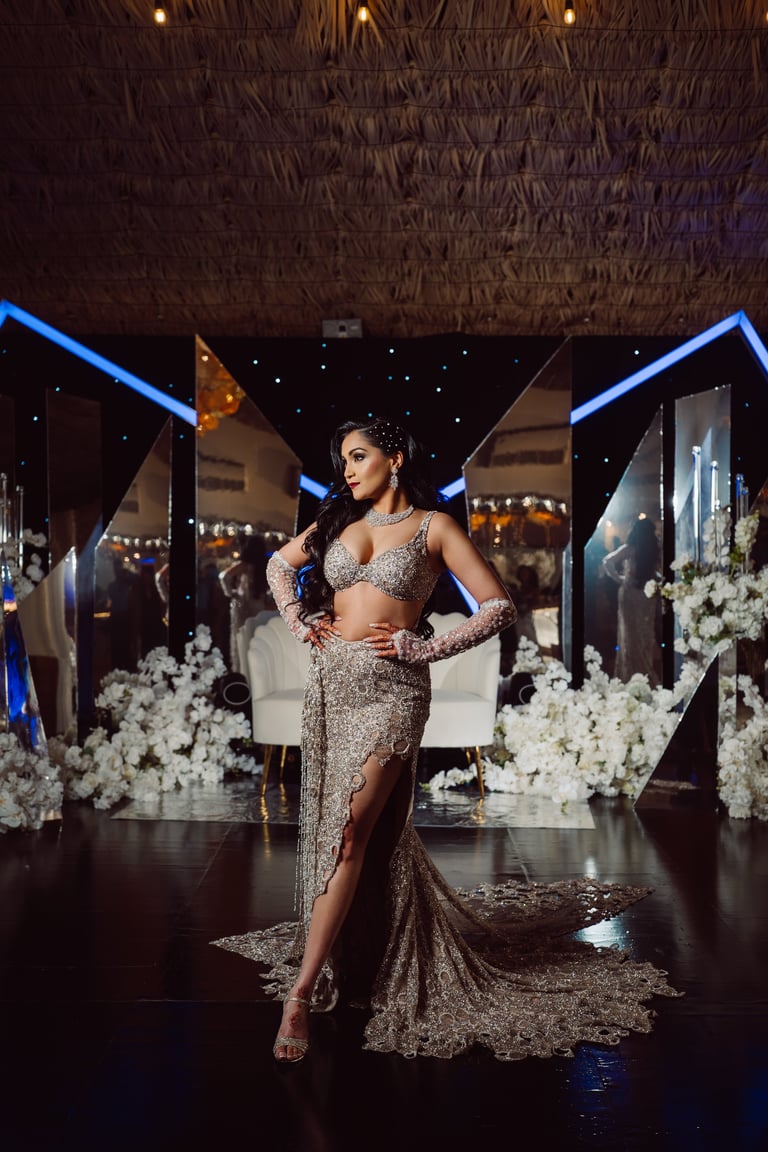 Woman in sparkly silver gown posing on stage with white flowers and blue neon lighting in background