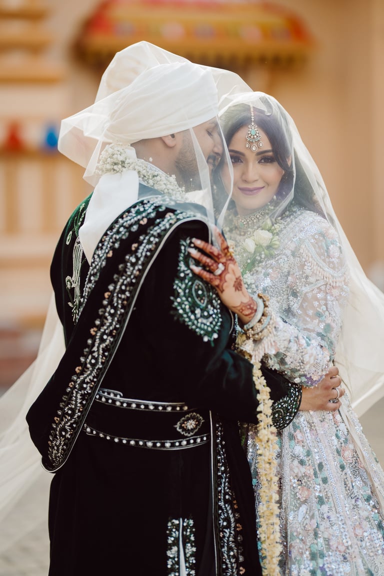 Bride and groom in traditional Islamic wedding attire, sharing an intimate moment under white veil with ornate embroidered garments