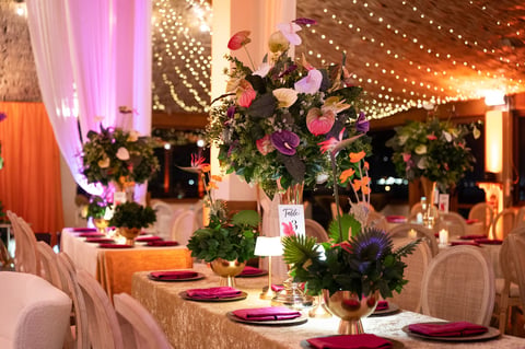 Elegant wedding reception venue with floral centerpieces, decorated tables, warm and pink lighting, and elegant place settings