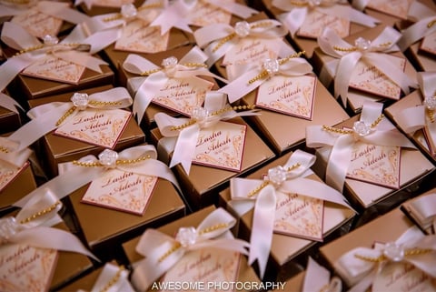 Gold wedding favors with personalized tags and white ribbons arranged in rows