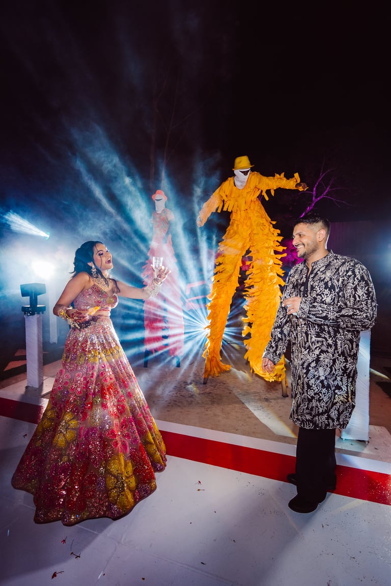 Couple in formal attire posing with illuminated yellow figure statue and dramatic blue lighting effects in background