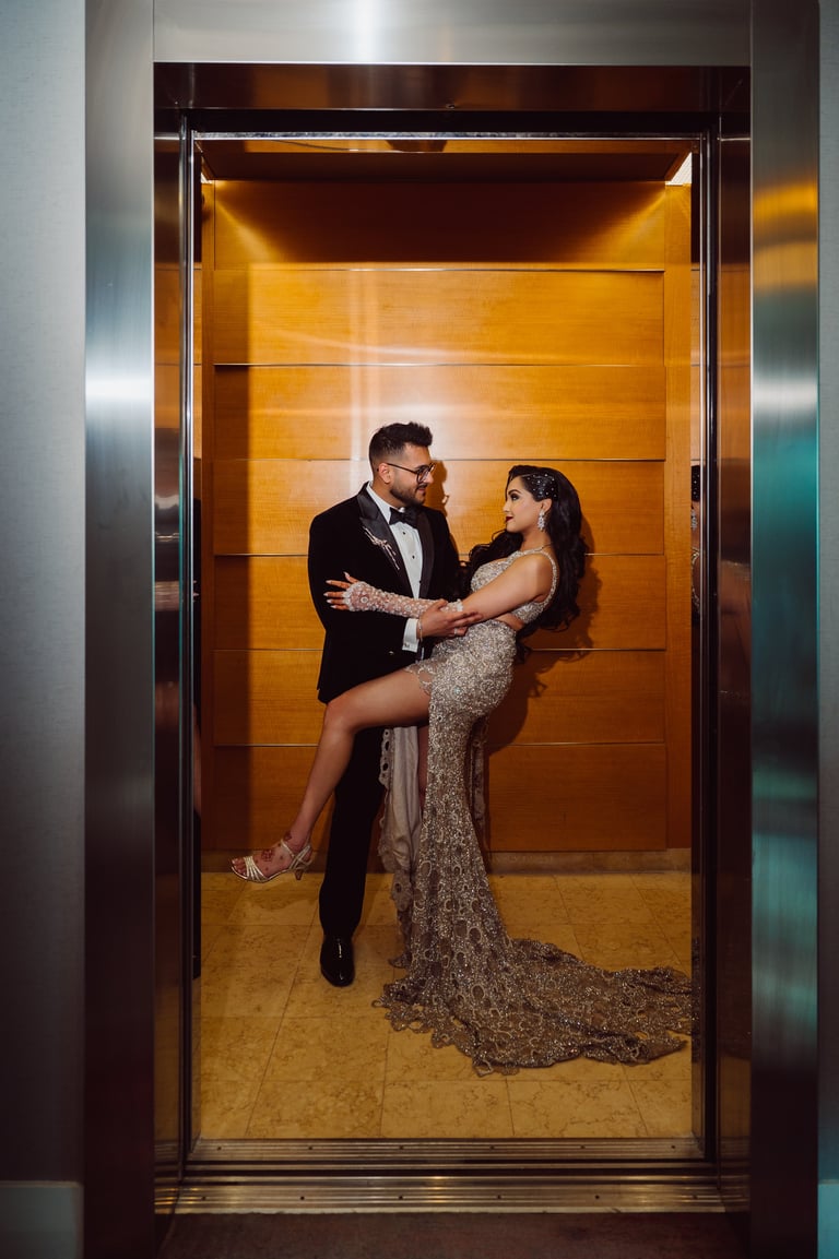 Couple in formal attire dancing in an elevator with gold-toned walls and metallic doors