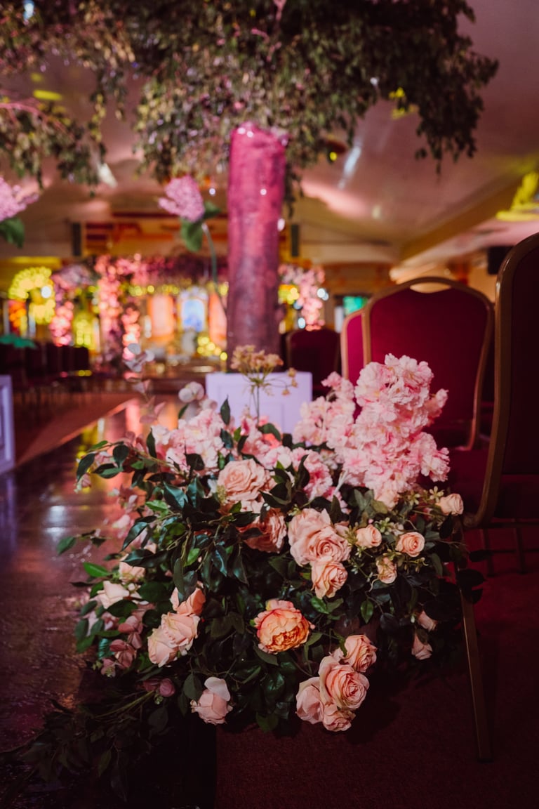 Elegant wedding venue decorated with pink roses and hanging greenery, illuminated by warm and colorful ambient lighting