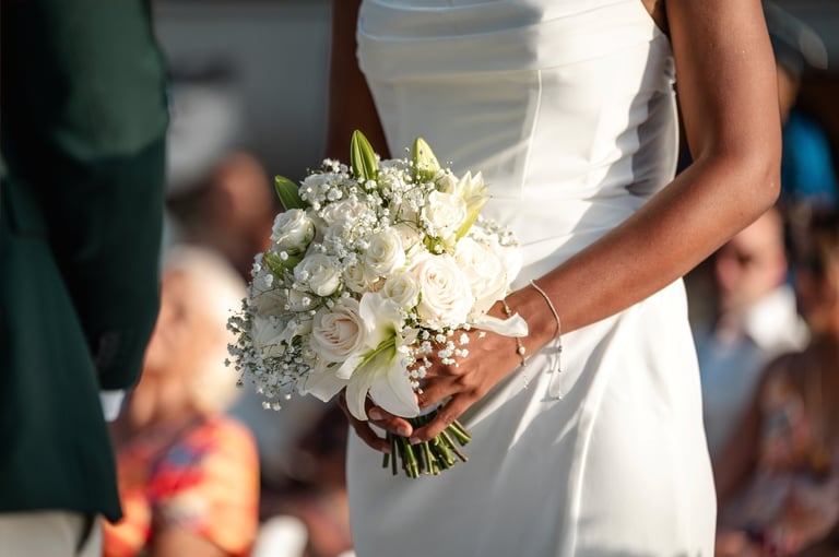 Bride in white wedding dress holding a bouquet of white flowers and greenery at outdoor ceremony