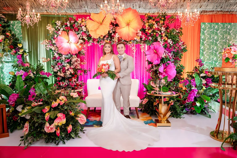 Couple at wedding ceremony with vibrant pink and orange floral decorations and neon pink backdrop