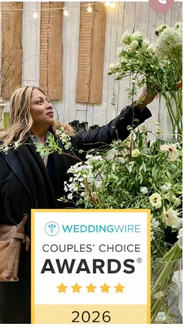 Woman in black blazer arranging white flowers next to a WeddingWire Couples Choice Awards 2026 sign with five gold stars
