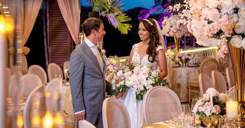 Bride and groom at elegant wedding reception with white floral arrangements and candlelit tables