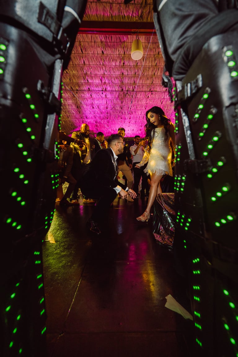People in formal attire standing in a neon-lit tunnel with vibrant pink and green lights creating a modern event venue atmosphere