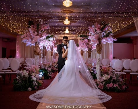 Bride and groom dancing under ornate chandelier in elegantly decorated wedding venue with pink flowers and draped ceiling