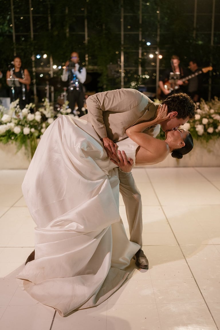 Groom dipping bride during their first dance at an outdoor evening wedding reception with band playing in background