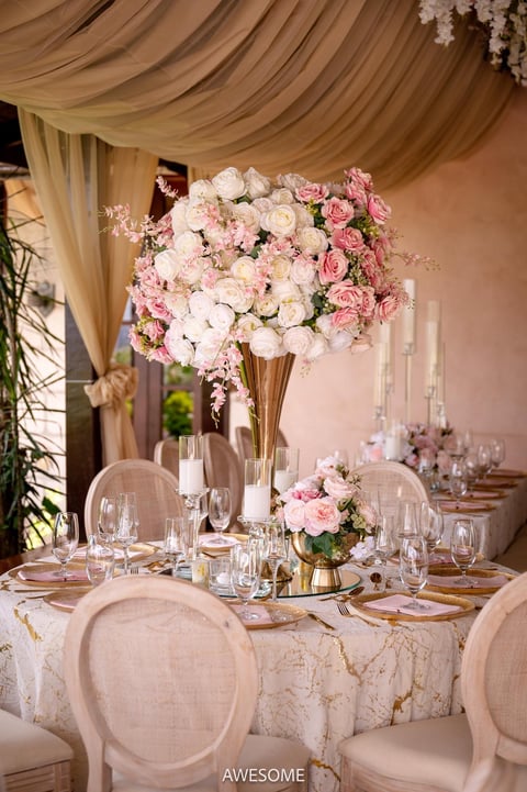 Elegant wedding table centerpiece with tall gold vase filled with pink and white roses and white hanging flowers above