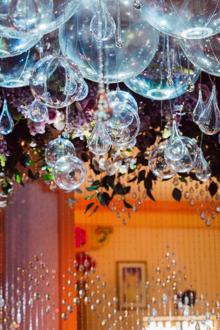 Hanging glass bubble ornaments and dewdrops suspended in air with colorful blurred background featuring warm orange and red tones