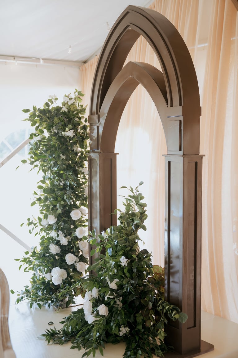 Tall wooden archway decorated with white flowers and green foliage in a bright, modern interior space