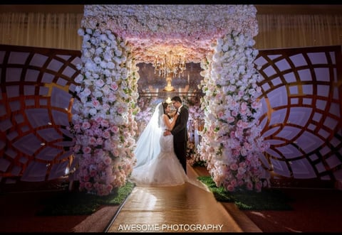 Bride and groom kissing under a grand floral archway decorated with white and pink flowers at an elegant wedding ceremony