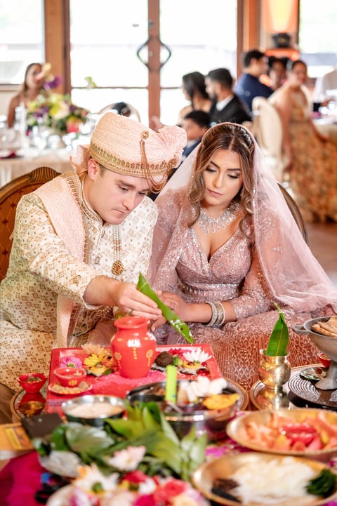 Bride and groom in traditional attire performing wedding ceremony ritual with flowers and candles at ornate venue
